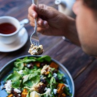 View from behind a person enjoying salad and tea at wooden table