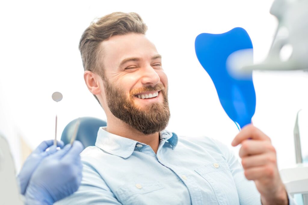 A man in a dentist’s chair looking in the mirror at his smile.